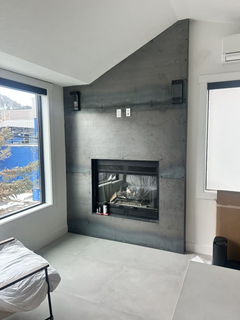 Blackened steel fireplace surround running floor to vaulted ceiling in a white bedroom