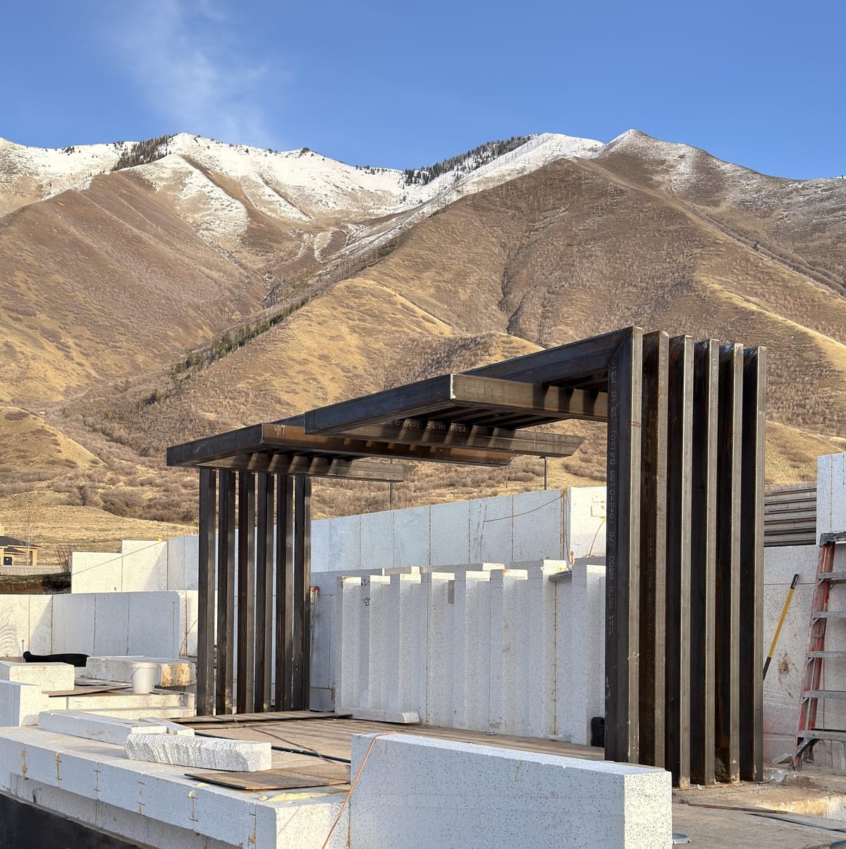 Raw steel pergola frame with fluted columns standing on a Utah job site below snow-covered mountains