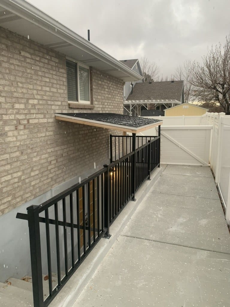 Black picket railing along a concrete side walkway beside a brick home on an overcast day
