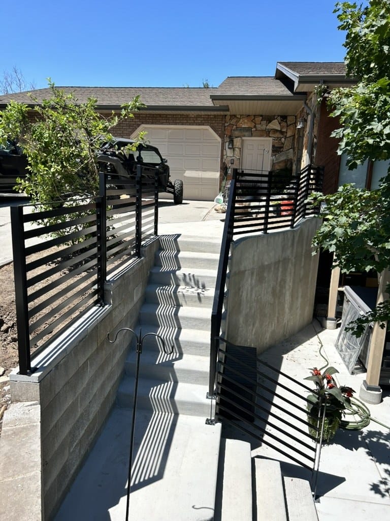 Black horizontal slat railing and privacy screen above a block retaining wall beside concrete entry steps