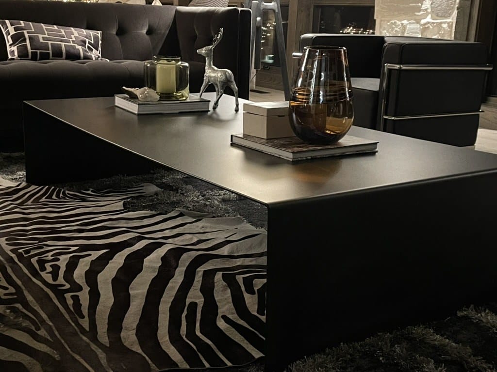 Low black steel waterfall-edge coffee table on a zebra-print rug in a dark modern living room